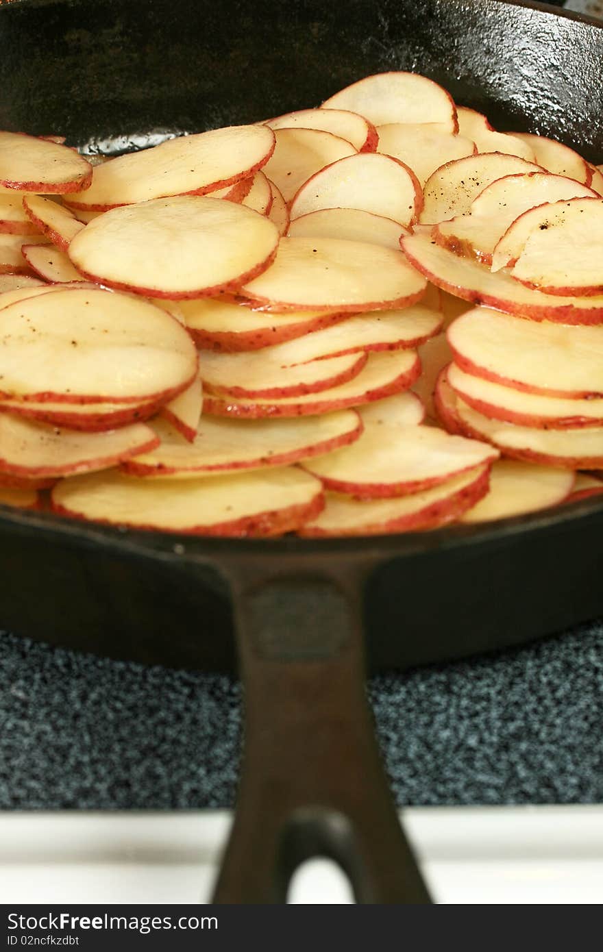 Sliced and seasoned potatoes in a cast iron skillet being fried/sauteed. Sliced and seasoned potatoes in a cast iron skillet being fried/sauteed.