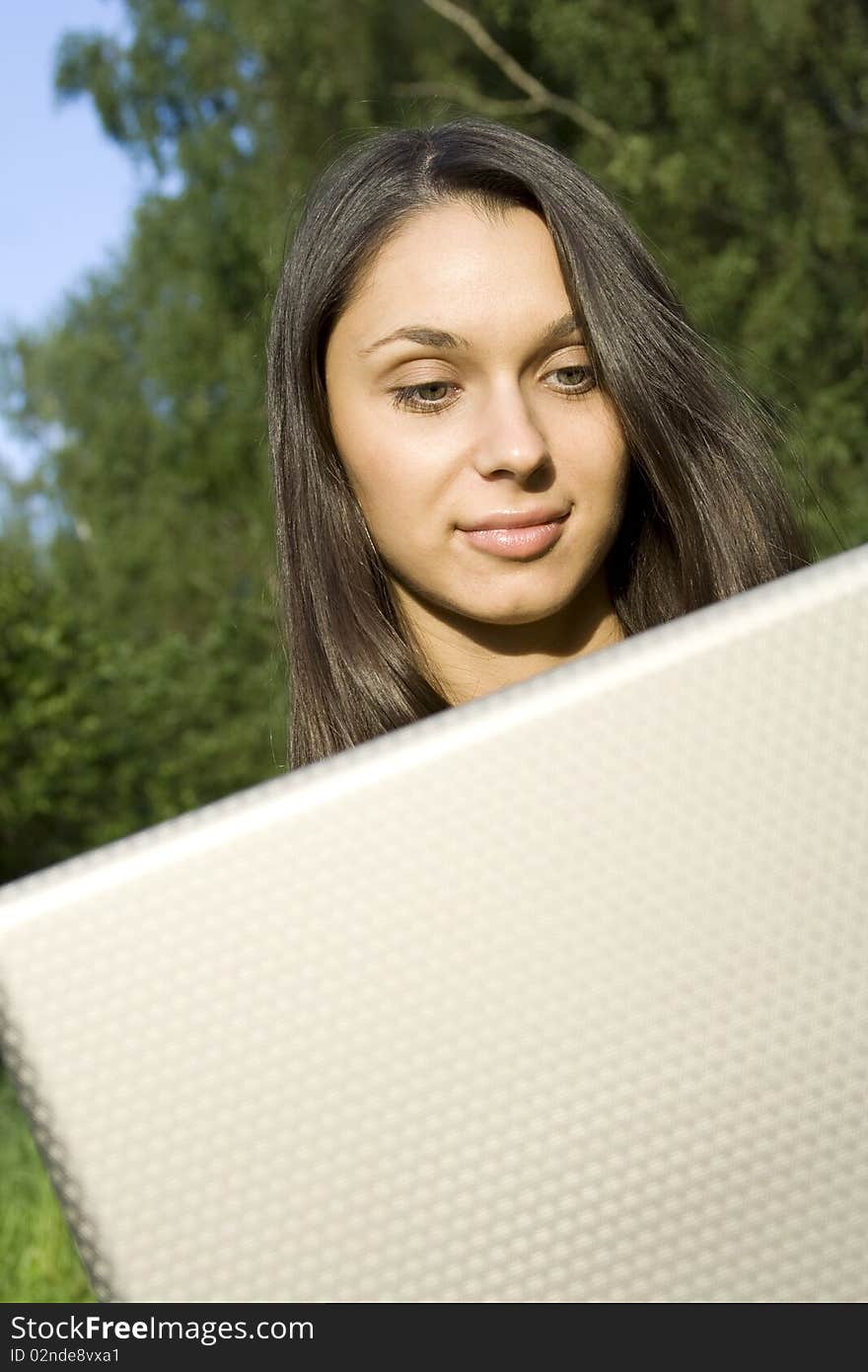 Young Caucasian woman with a laptop in the park on a green grass / meadow