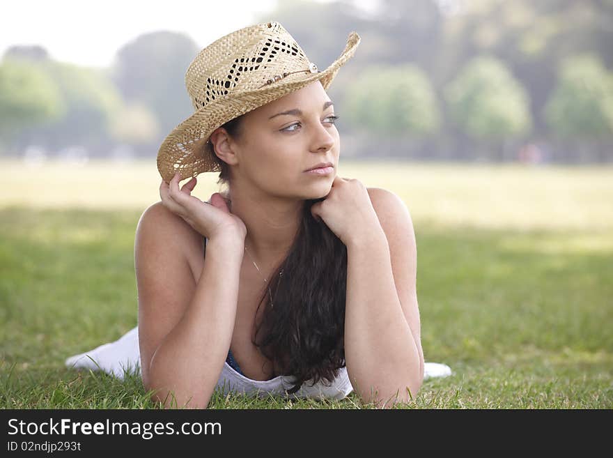 Young attractive girl lying on grass contemplating while wearing a summer hat. Young attractive girl lying on grass contemplating while wearing a summer hat