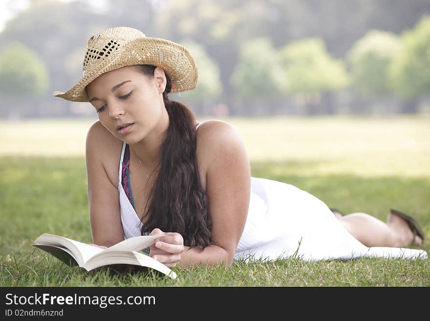 Young attractive girl lying on grass while reading a book. Young attractive girl lying on grass while reading a book