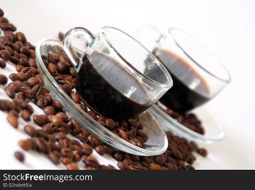 Two coffee cups made by transparent glass in diagonal with a lot of coffee beans. Two coffee cups made by transparent glass in diagonal with a lot of coffee beans