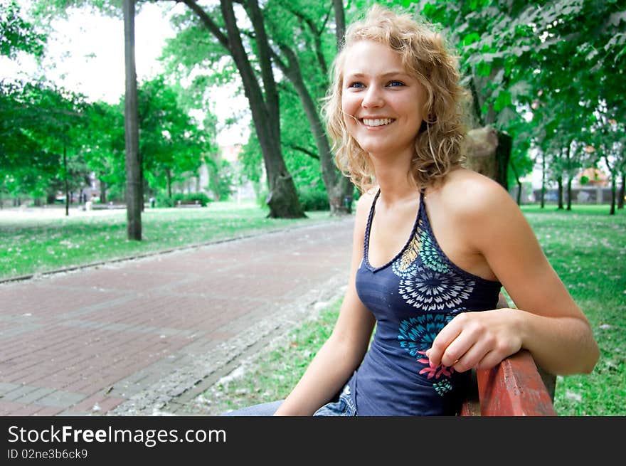 Young beautiful girl sitting on a park bench and smiles. Young beautiful girl sitting on a park bench and smiles.