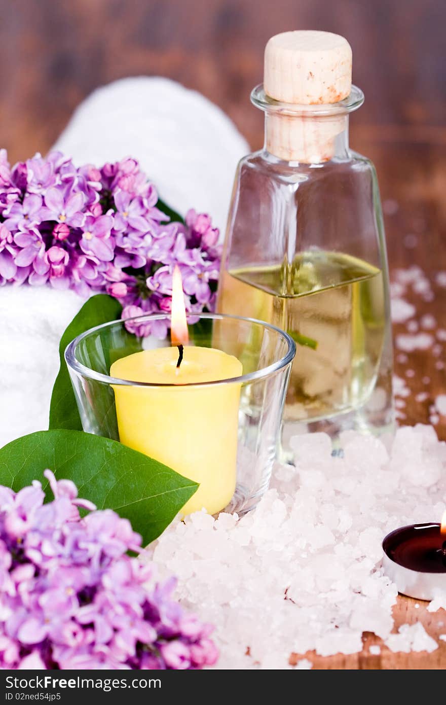 Bath and spa items (towel, salt, oil, lilac, candle) on wooden background