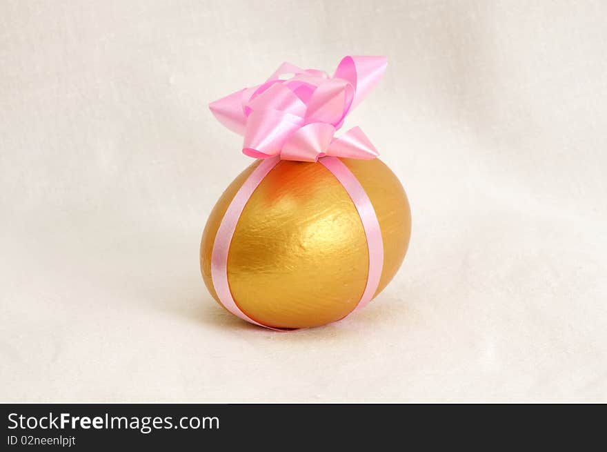 A golden egg wrapped in pink ribbon with a white fabric as background