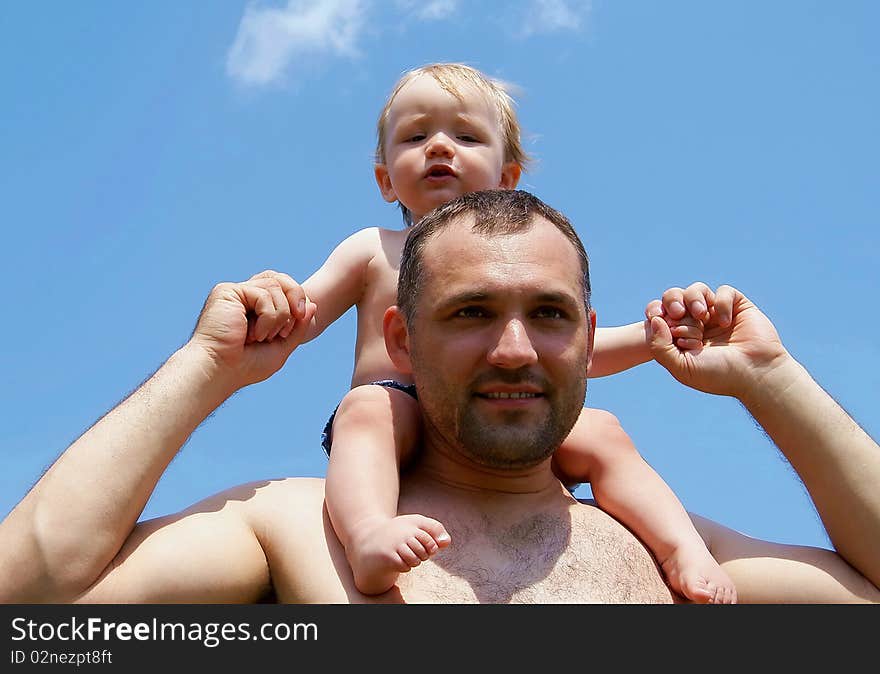 In the summer against the sky the man holds the kid for hands having put to itself on shoulders. In the summer against the sky the man holds the kid for hands having put to itself on shoulders