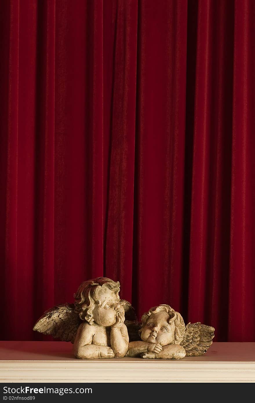 Sculptures of two small cupids on a red background look upwards. Sculptures of two small cupids on a red background look upwards