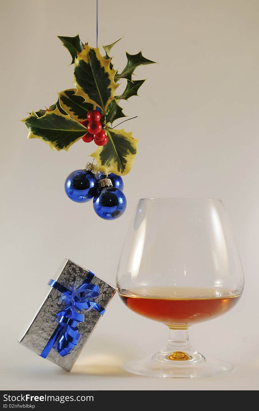 Brandy snifter with silver present under holly with red berried and blue bulbs. Brandy snifter with silver present under holly with red berried and blue bulbs