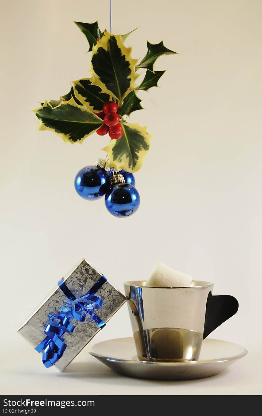 Cup and saucer of cocoa with marshmellow with gift under holly with blue bulbs. Cup and saucer of cocoa with marshmellow with gift under holly with blue bulbs