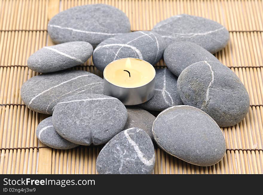 A light candle and pebbles on bamboo mat. A light candle and pebbles on bamboo mat