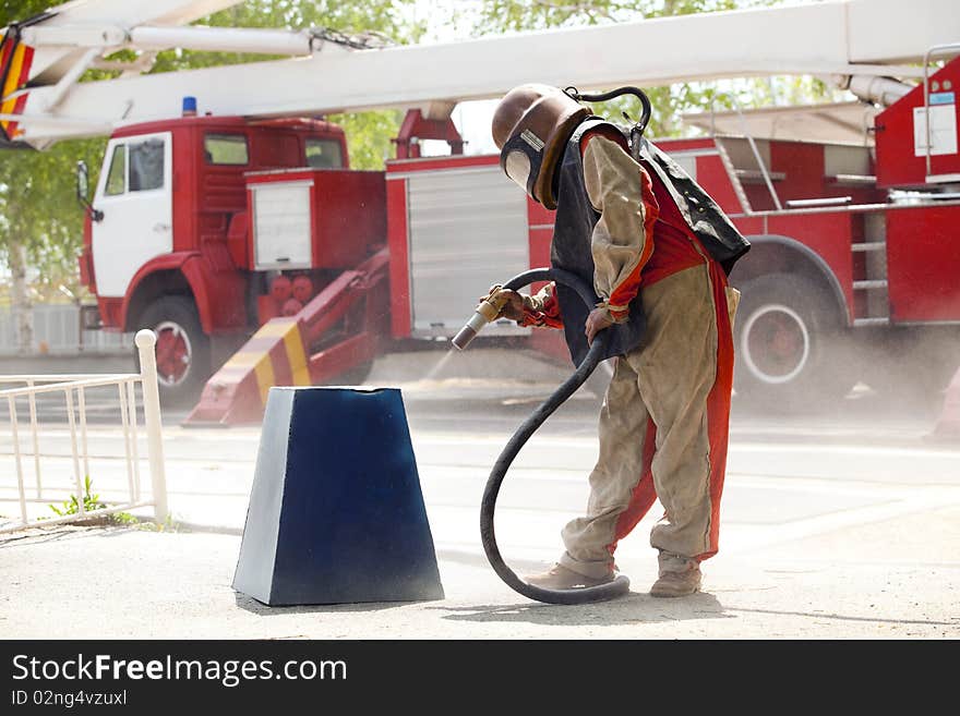 Worker in a protective suit spraying sand with abrasive peeler