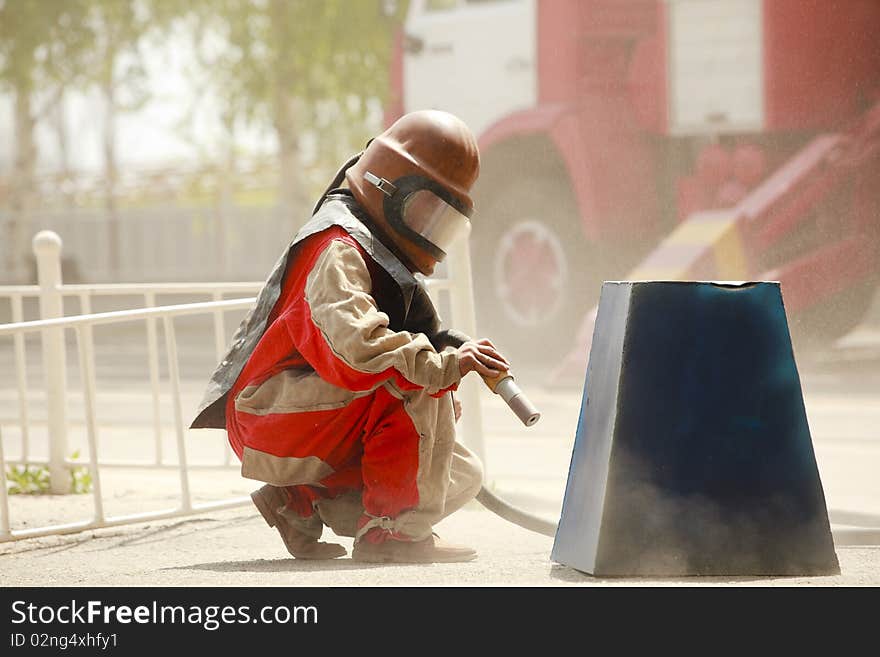 Worker in a protective suit spraying sand with abrasive peeler