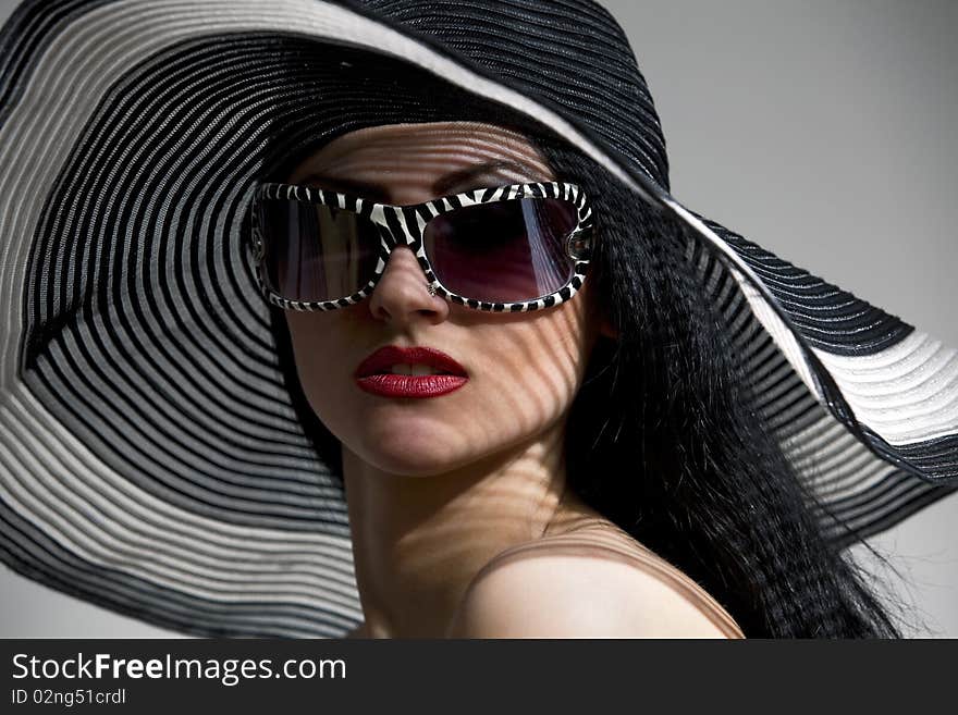 Beautiful model in striped hat and top with glassses on the gray  background