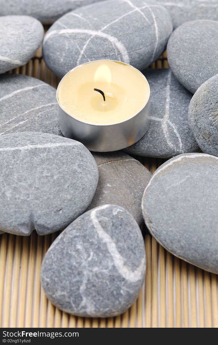 A light candle and pebbles on bamboo mat. A light candle and pebbles on bamboo mat