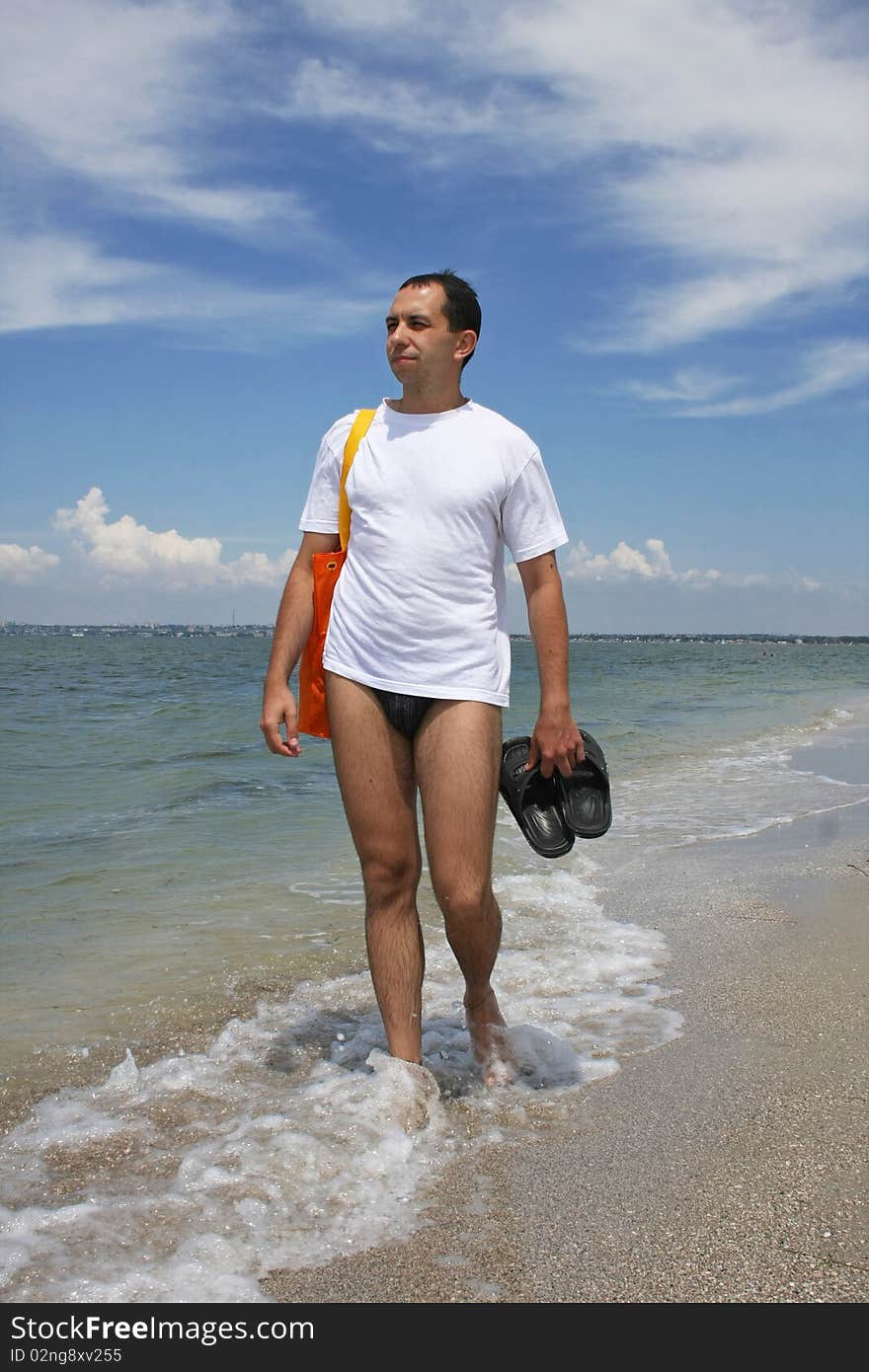 A man in a white sport shirt goes for a walk on a beach. A man in a white sport shirt goes for a walk on a beach