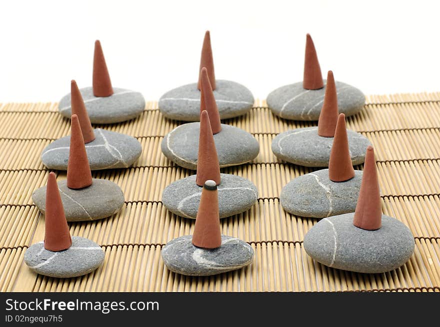 A row of incense cones over pebbles on bamboo mat. A row of incense cones over pebbles on bamboo mat