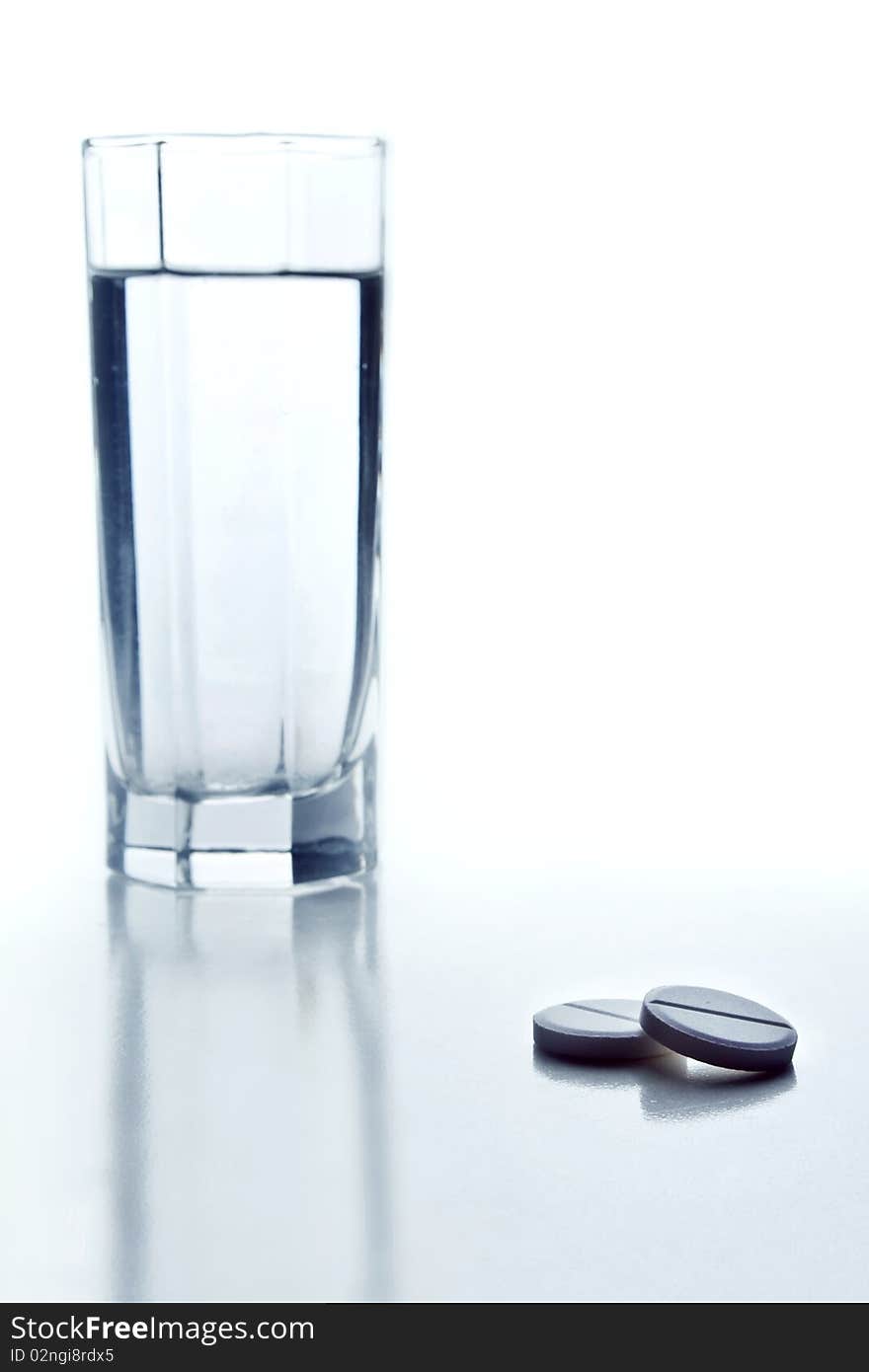 Two tablets and glass of water on white background. Two tablets and glass of water on white background