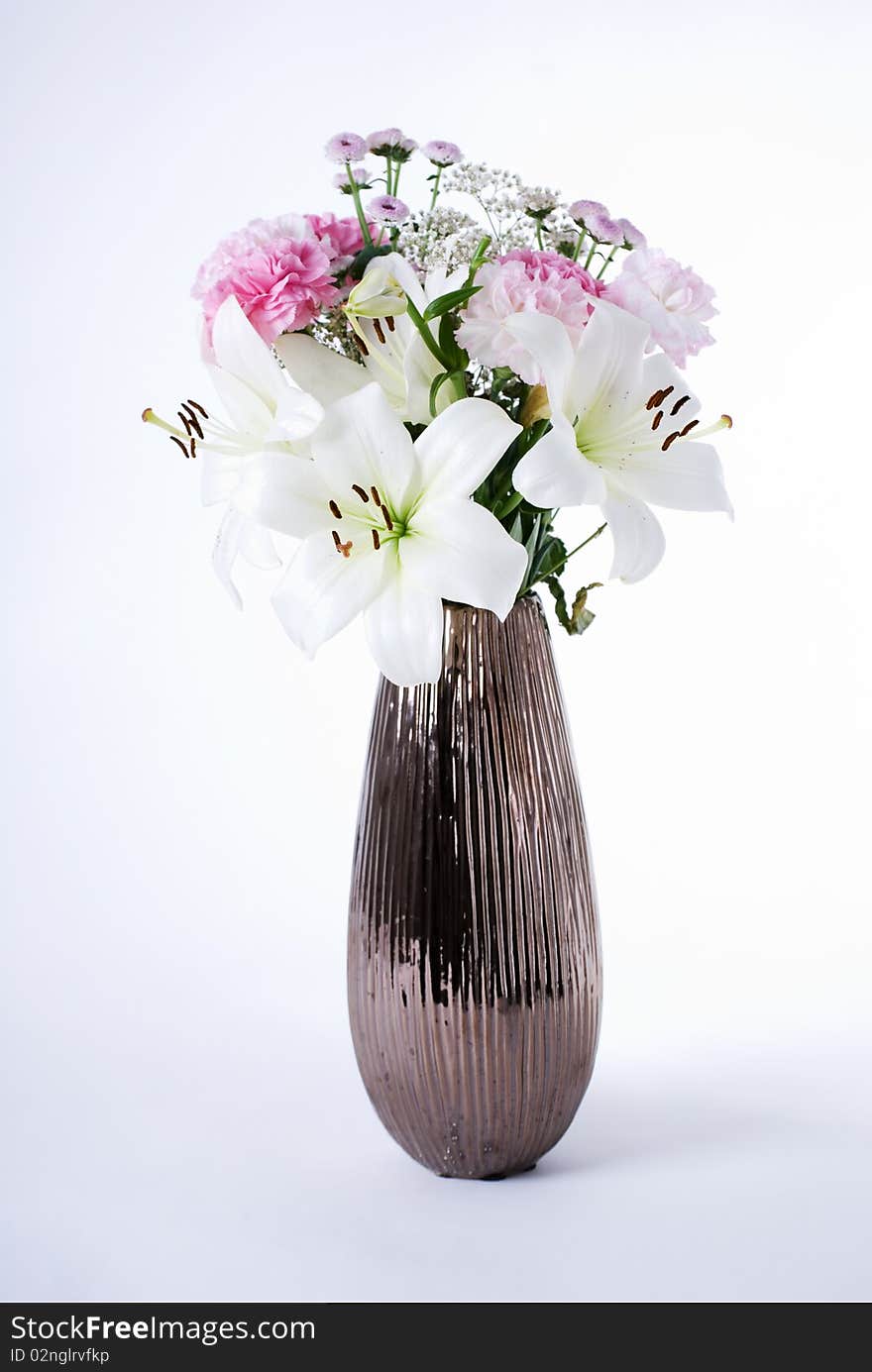 A flower arrangement of carnations and lillies in a brown metallic vase. A flower arrangement of carnations and lillies in a brown metallic vase