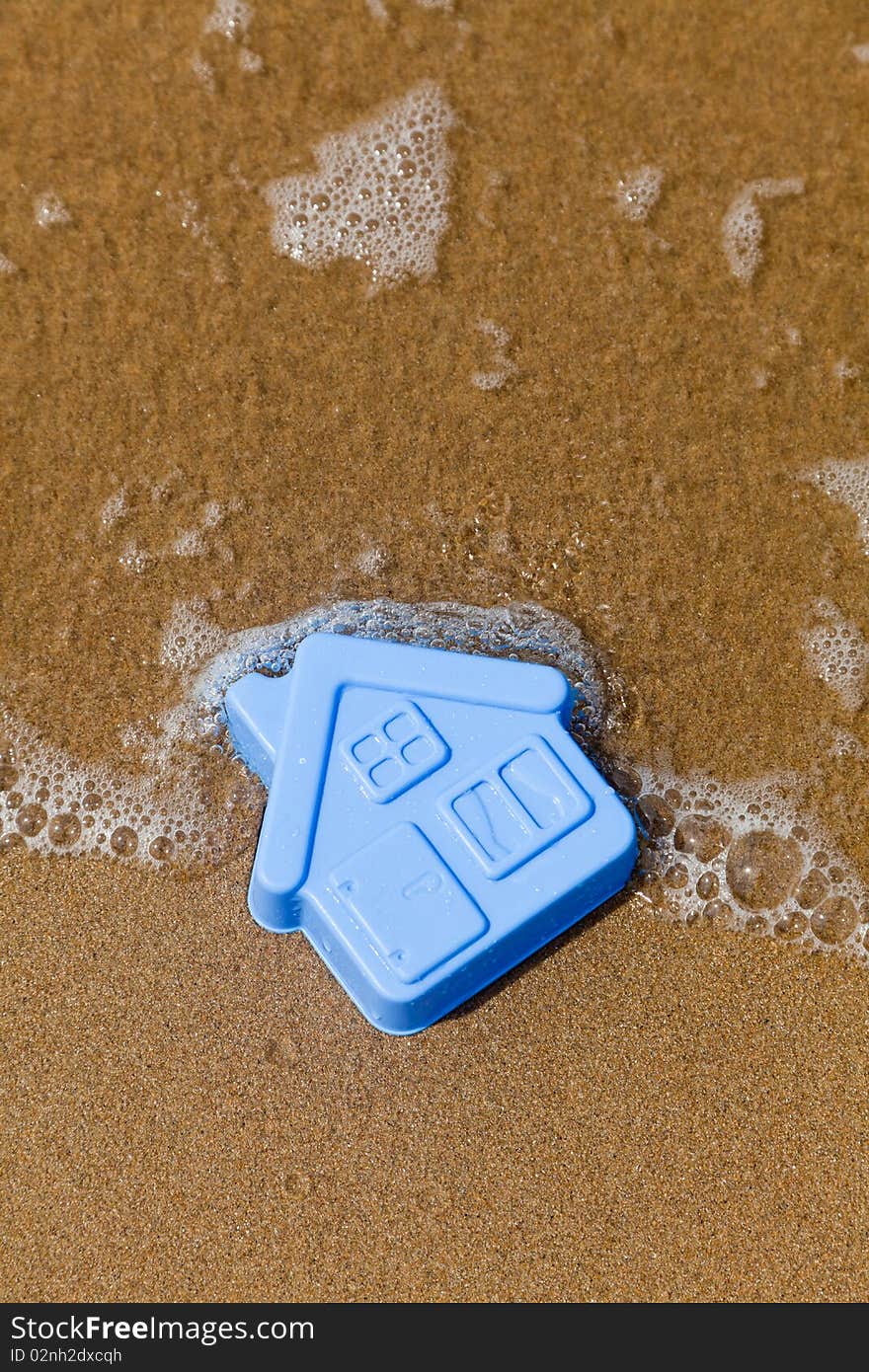 Blue toy plastic house on the sand washes wave. Blue toy plastic house on the sand washes wave