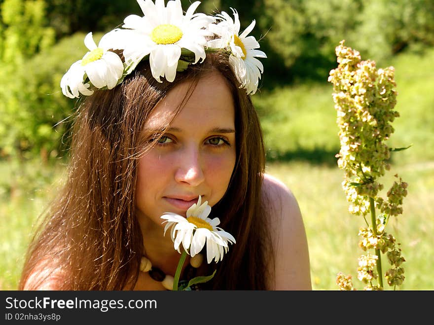 Charming young woman in garland white field camomile upon green meadow