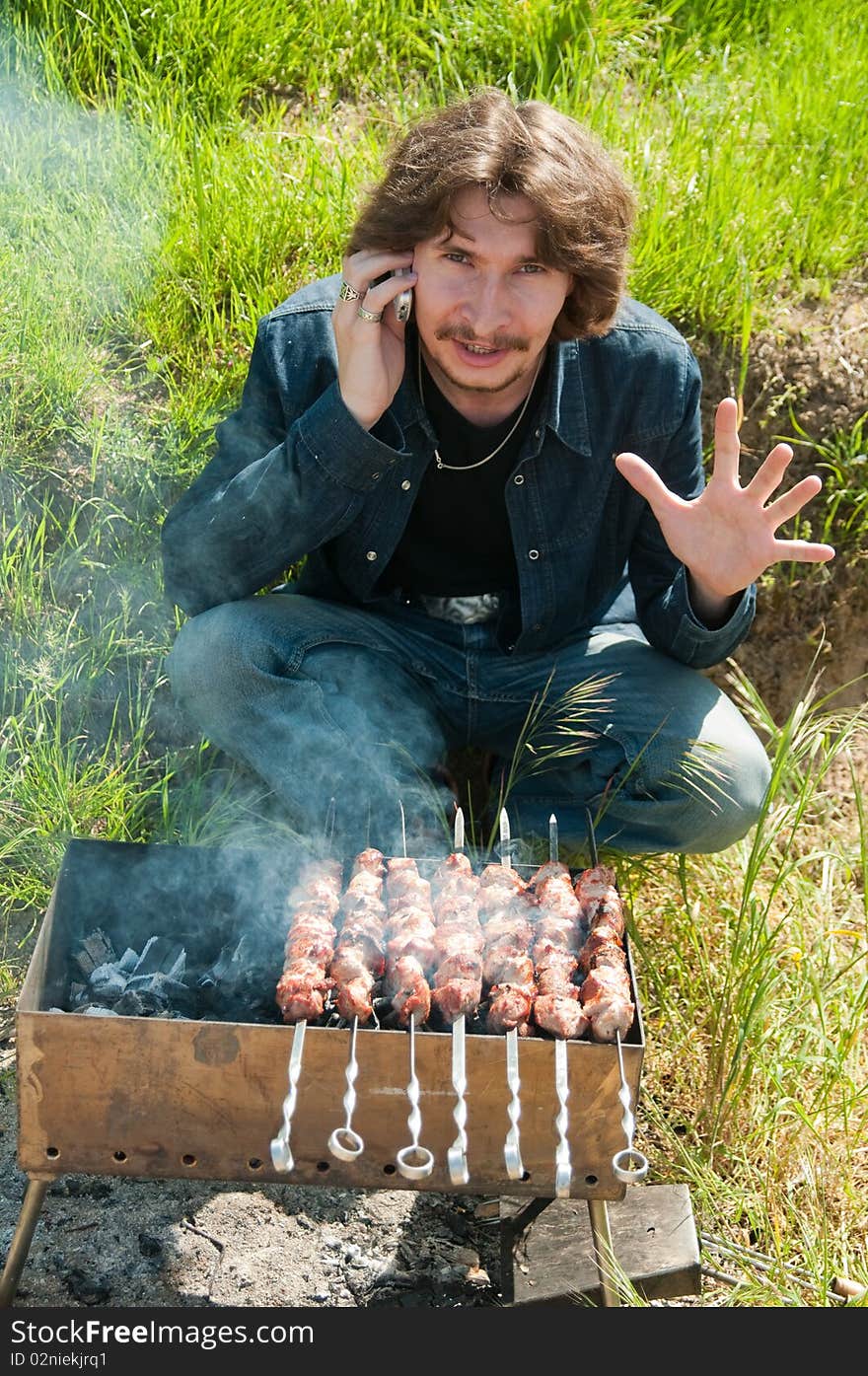 The man sits at a brazier on which the shish kebab prepares. The man sits at a brazier on which the shish kebab prepares.