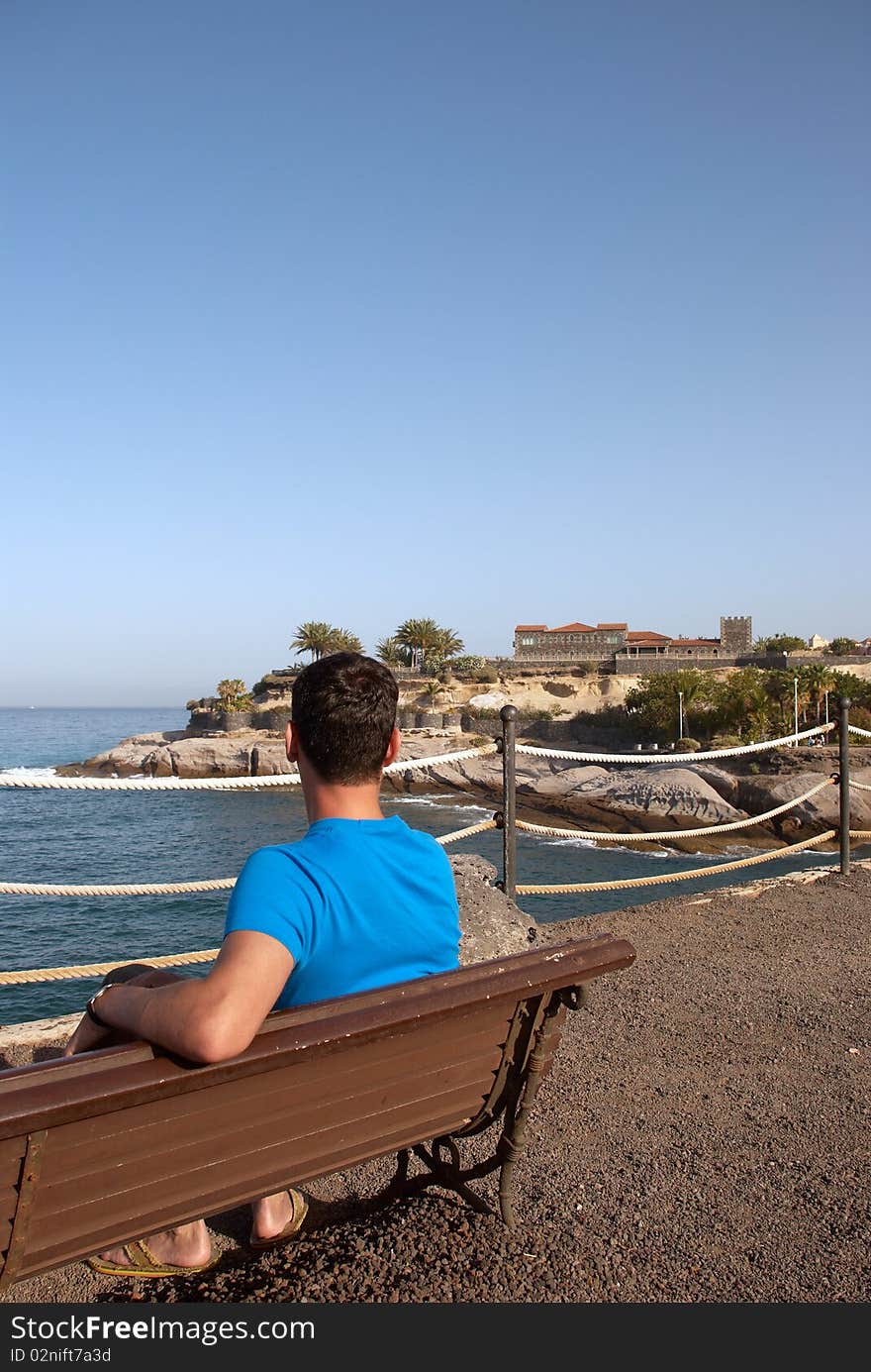 Young man sitting alone on a bench and looking out to the ocean. Young man sitting alone on a bench and looking out to the ocean