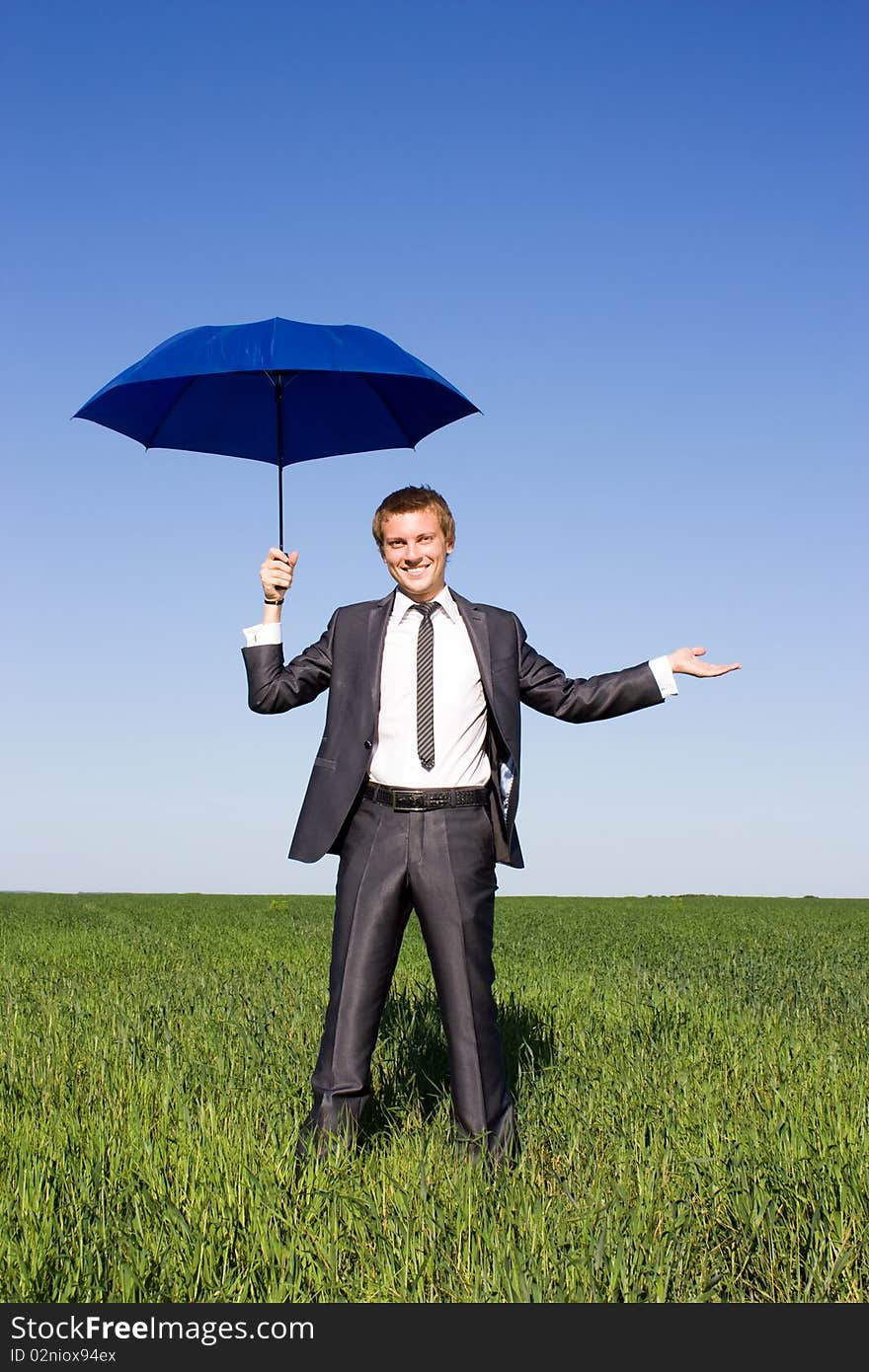 Businessman with blue umbrella in field