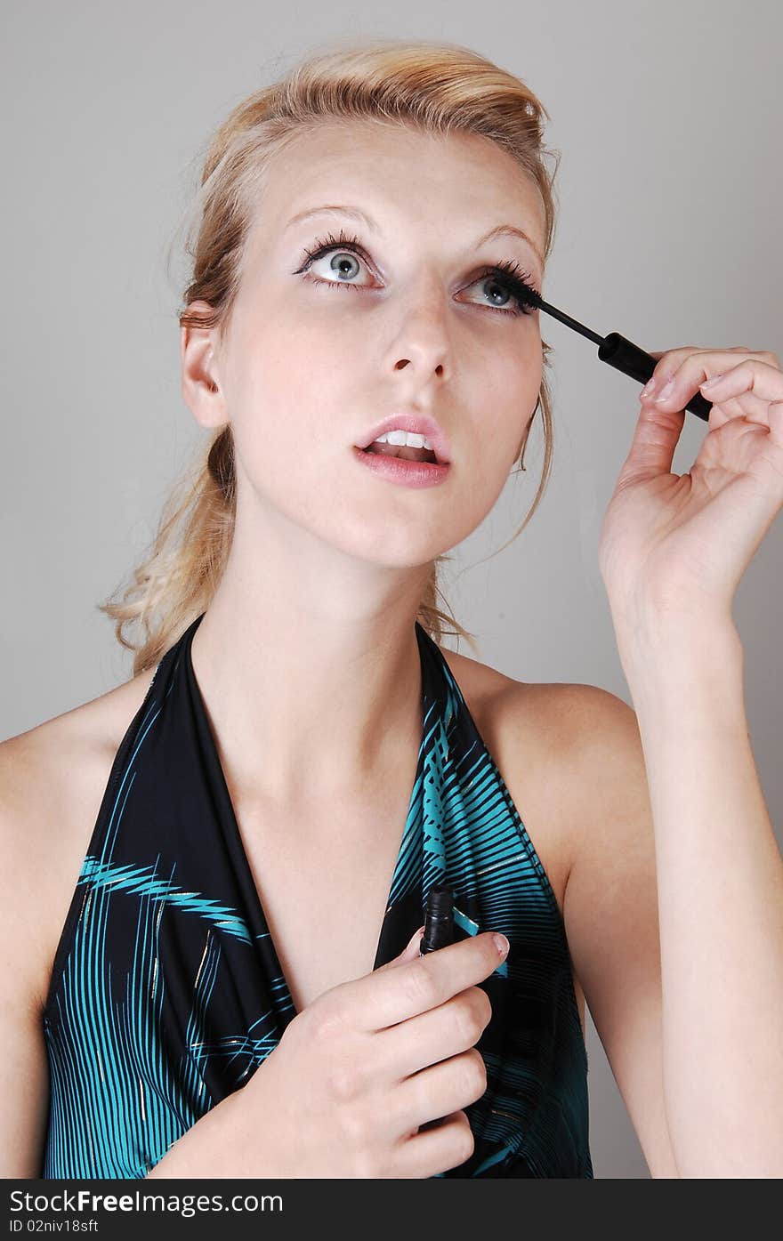 A beautiful blond woman in closeup, doing her makeup and fixing her
eyelashes, looking up, for light gray background. A beautiful blond woman in closeup, doing her makeup and fixing her
eyelashes, looking up, for light gray background.