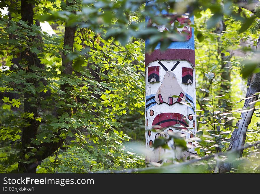 A colorful, painted totem pole amongst the trees in a green forest. A colorful, painted totem pole amongst the trees in a green forest.