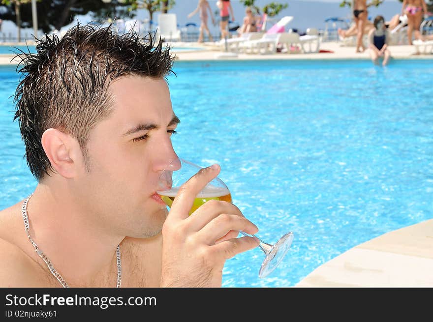 Young man drinking glass of beer at the swimming pool