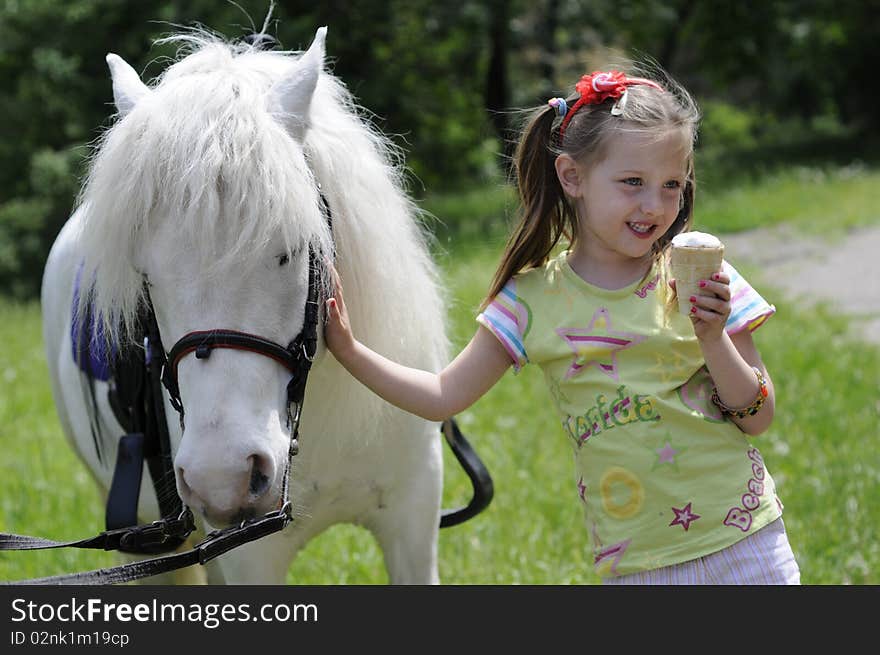 Small white horsy and the little girl with ice-cream, a green lawn. Small white horsy and the little girl with ice-cream, a green lawn