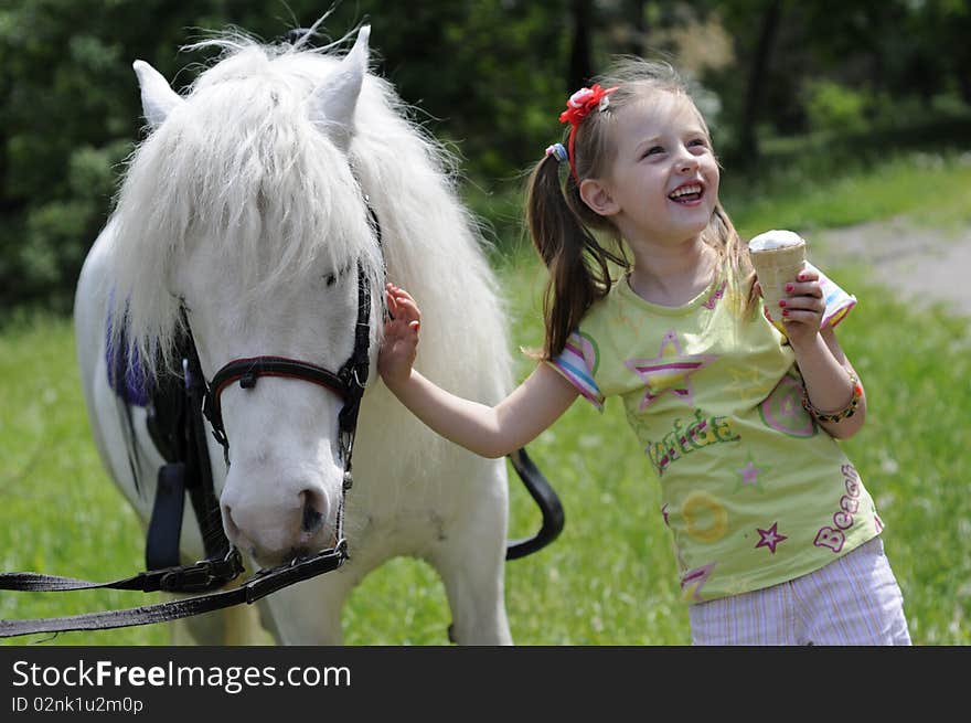 Small white horsy and the little girl with ice-cream, a green lawn. Small white horsy and the little girl with ice-cream, a green lawn