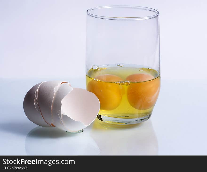 Two broken eggs in a glass and shells on a blue background