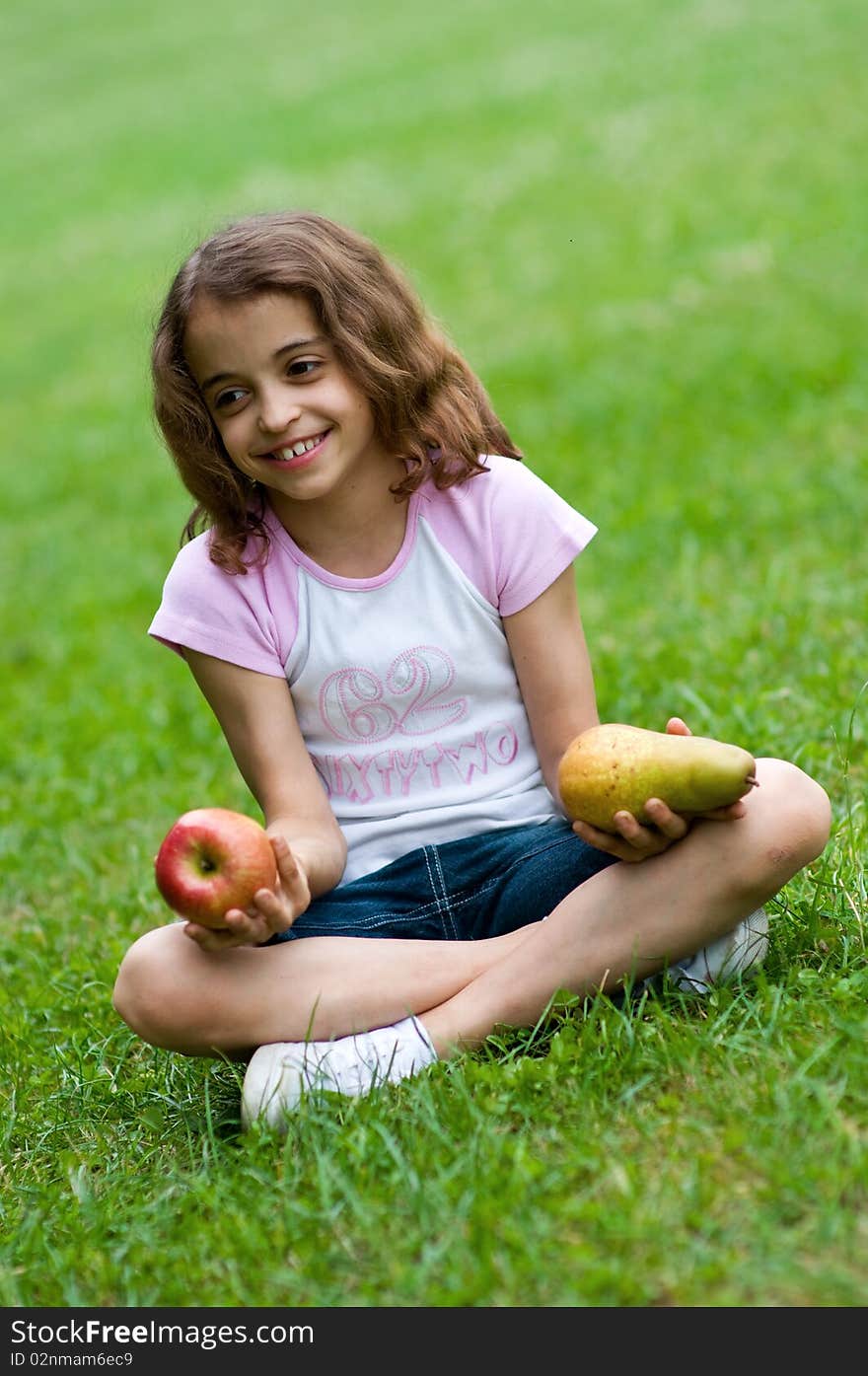 Portrait of a preteen girl with an apple and a plum in her hands and green grass in the background. Portrait of a preteen girl with an apple and a plum in her hands and green grass in the background