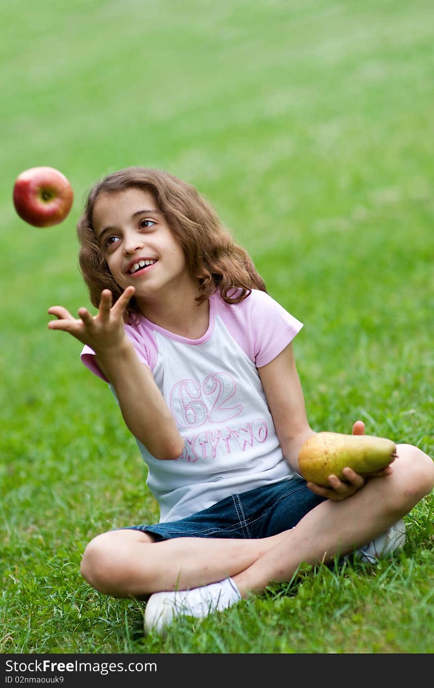 Portrait of a preteen girl trowing apple in the air and with a plum in her other hand and green grass in the background. Portrait of a preteen girl trowing apple in the air and with a plum in her other hand and green grass in the background