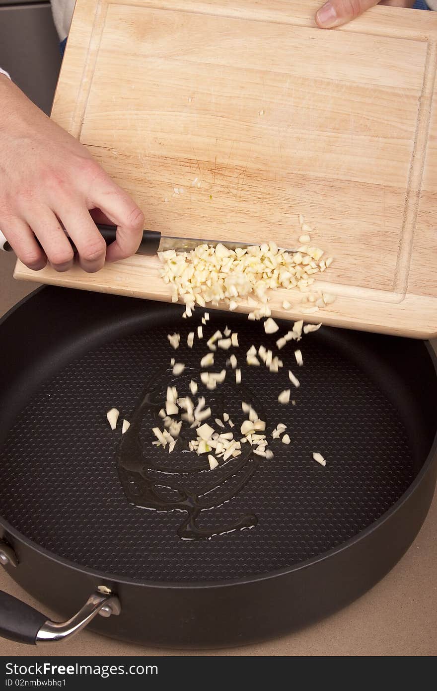 Chef pouring garlic pieces into frying pan. Chef pouring garlic pieces into frying pan