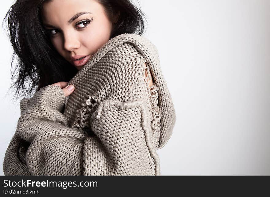 Portrait of Beautiful young brunette in a woollen sweater pose on a grey background in studio. Photo with copyspace.