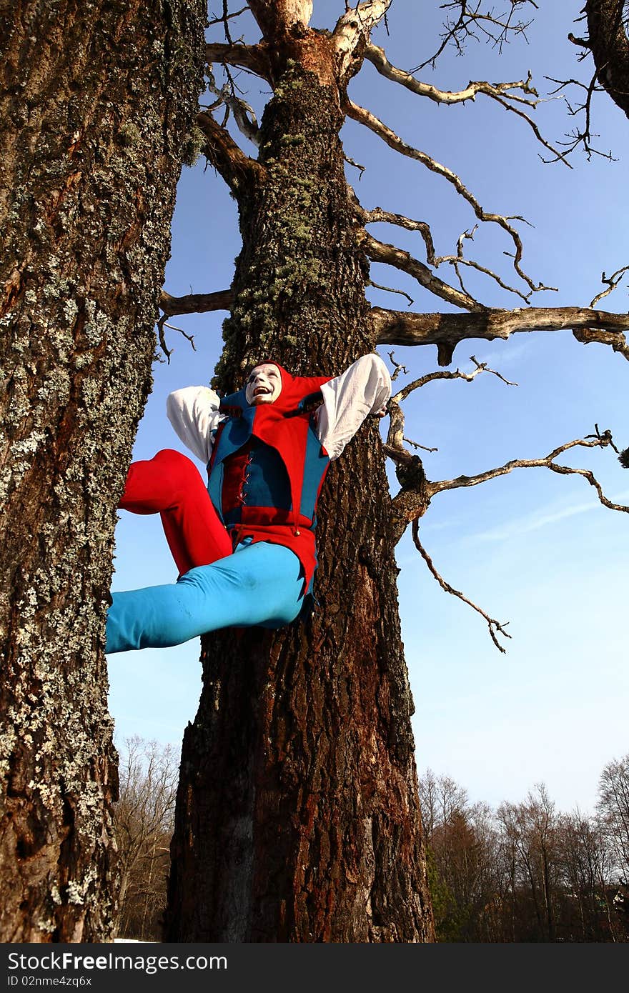 Artistic man in a suit of fire-clown rotate a fiery chain posing on backround of forest. Outdoor photo.