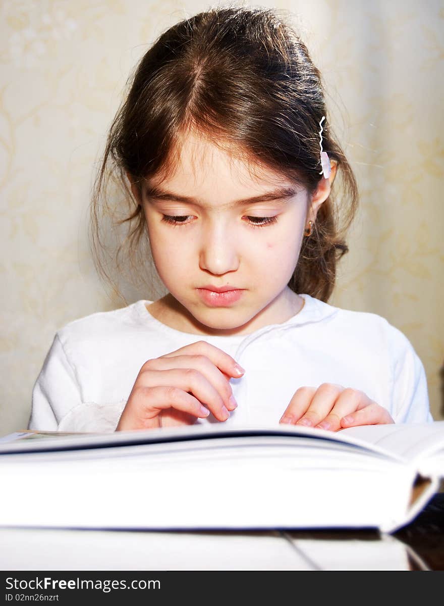 Young school girl reading book at home