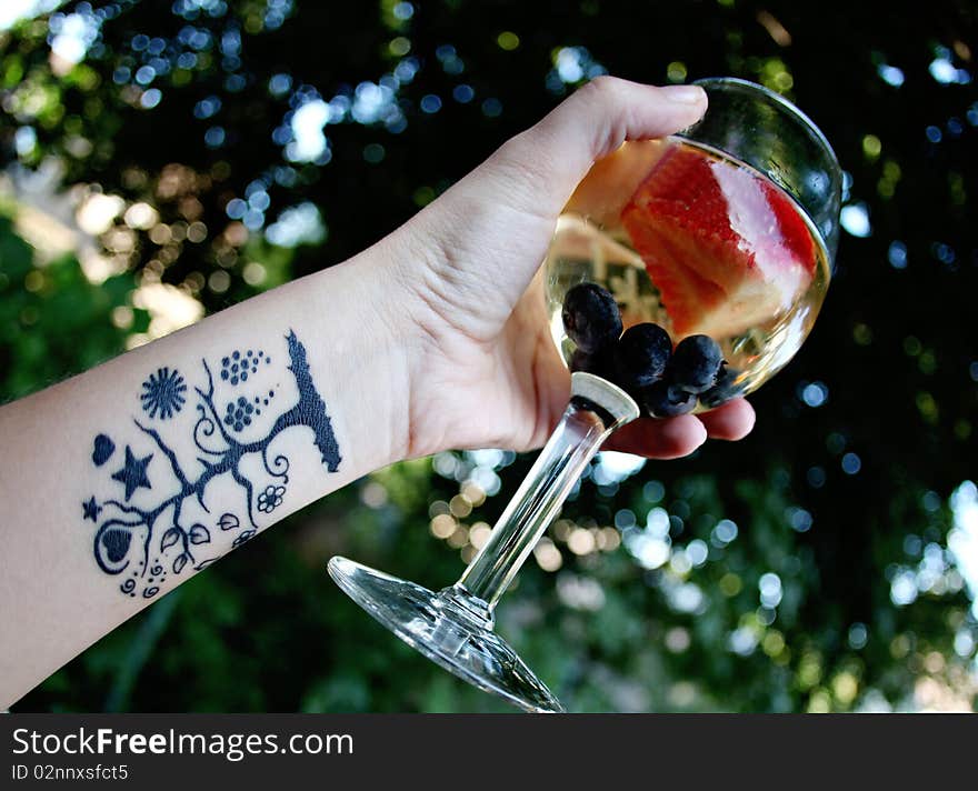 A glass of white sangria in a female's hand with a tree tattoo on her arm.