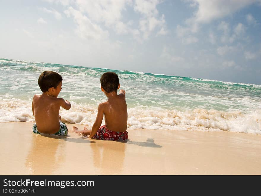 Two boys playing at the sea sitting on the sand