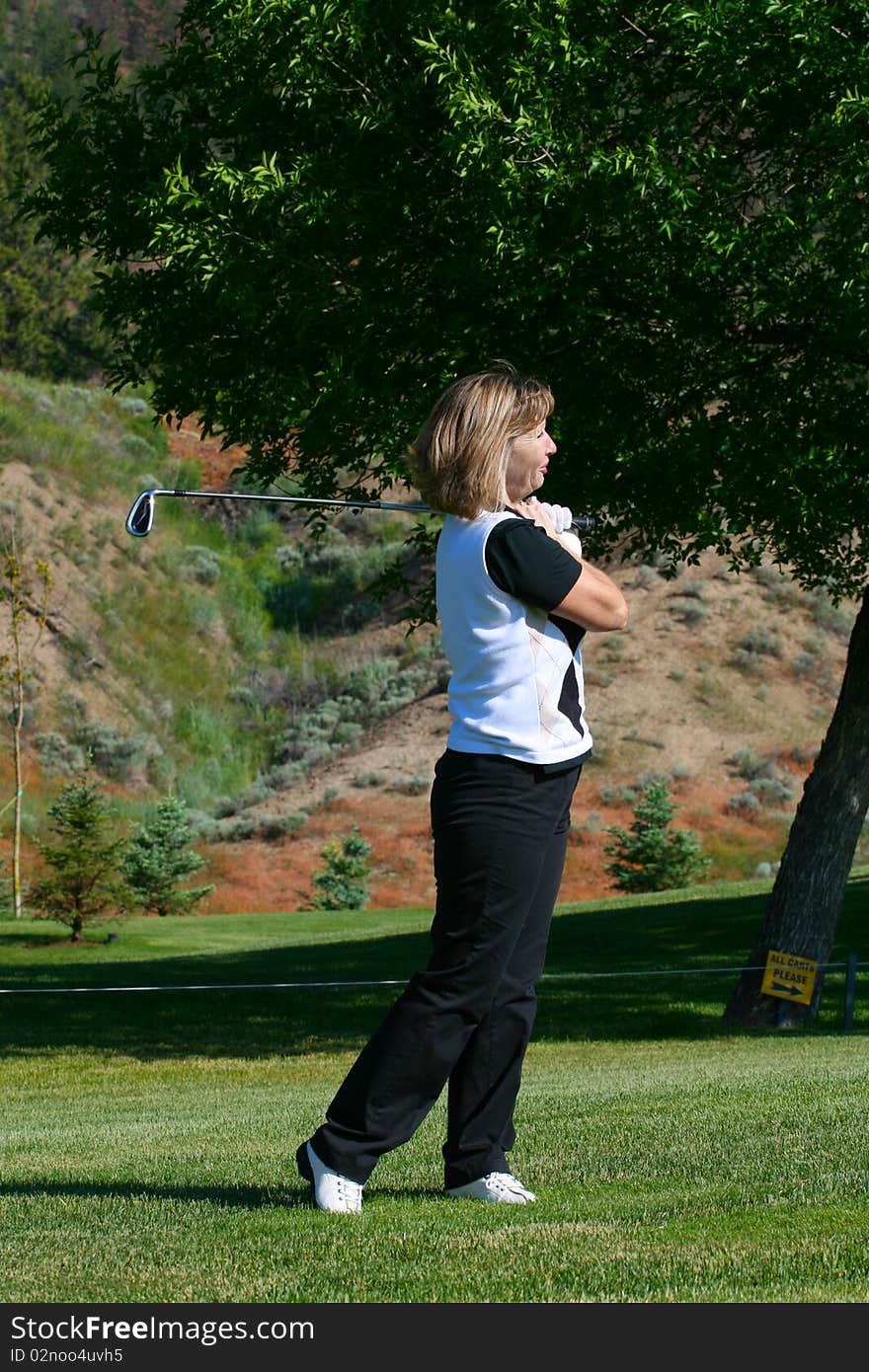 Blond female golfer following her ball down the fairway