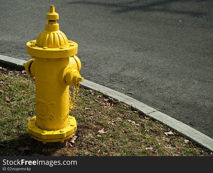 Looking down at a bright yellow fire hydrant siitting next to a squared curb as it divides the street and dismal grass and leaves of the fall season. Looking down at a bright yellow fire hydrant siitting next to a squared curb as it divides the street and dismal grass and leaves of the fall season.