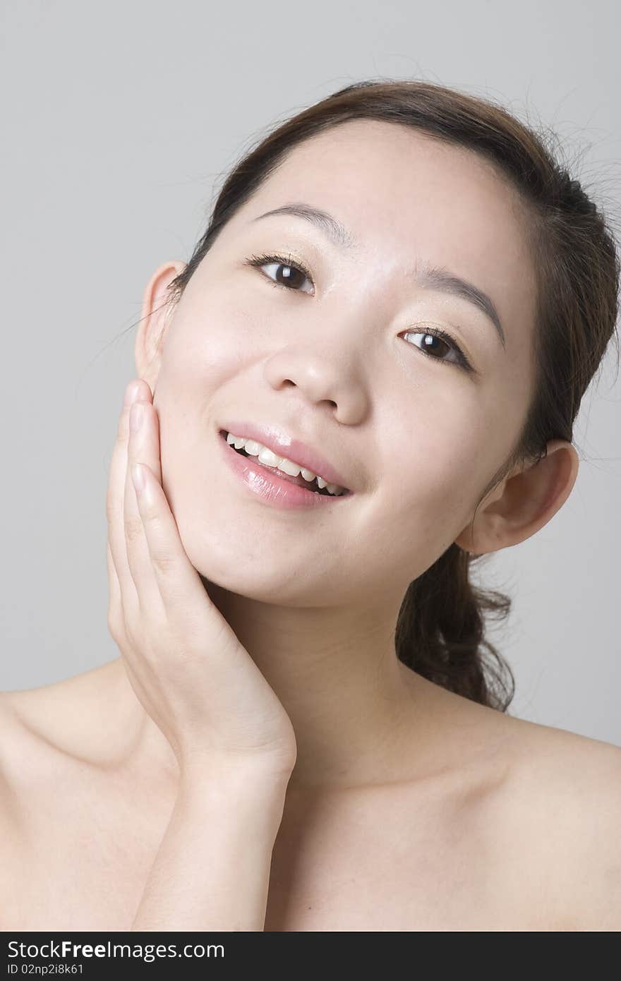 A smiling Asian girl with her hand touching her chin, taken in studio, for skin protection, beauty saloon, cosmetics advertisement use. A smiling Asian girl with her hand touching her chin, taken in studio, for skin protection, beauty saloon, cosmetics advertisement use.