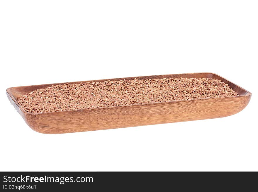 Grains of buckwheat groats in a wooden long plate on a white background.