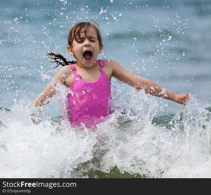 Little girl laughing and crying in the spray of waves at sea on a sunny day