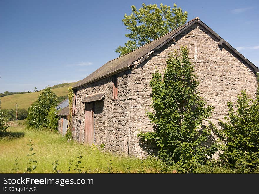 An old stone barn in a sunlit field against blue skies