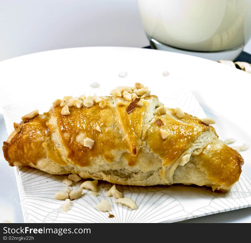 Small croissant on a white plate with napkin and a glass of milk in the background. Small croissant on a white plate with napkin and a glass of milk in the background