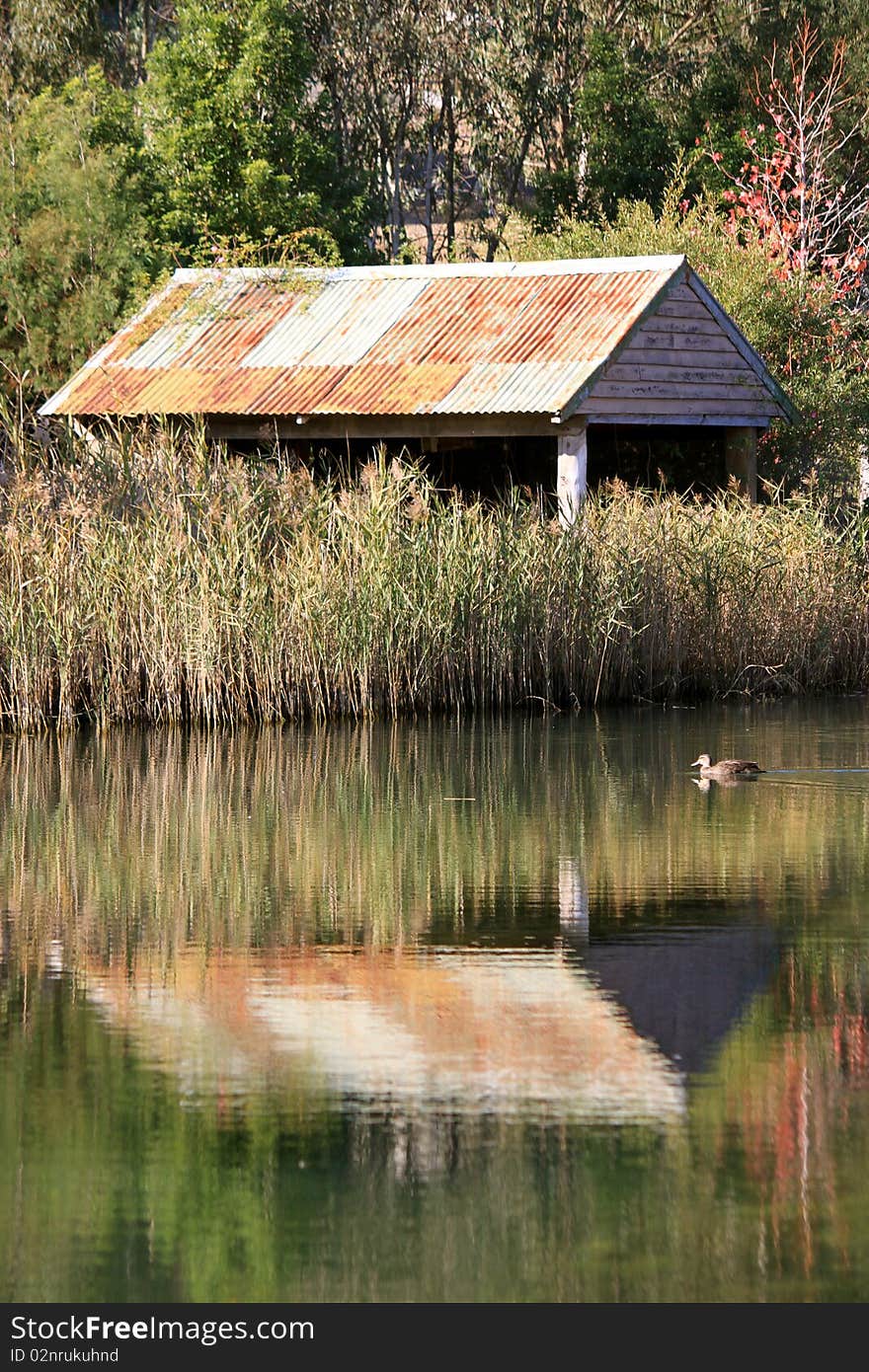 A rustic old shed in a rural area reflects in the afternoon sunlight onto a lake. A rustic old shed in a rural area reflects in the afternoon sunlight onto a lake.