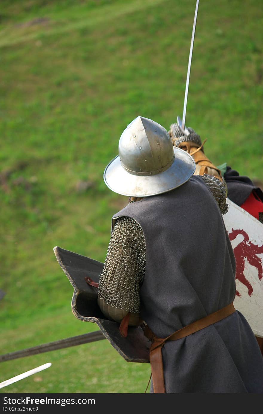 Medieval knight with metal helmet and sword running towars enemy in battlefield. The armored man in the photo is photographed from behind. Medieval knight with metal helmet and sword running towars enemy in battlefield. The armored man in the photo is photographed from behind.