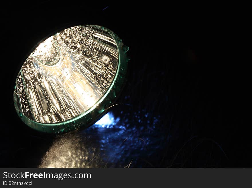 Closeup of luminous flashlight and water drops on dark background